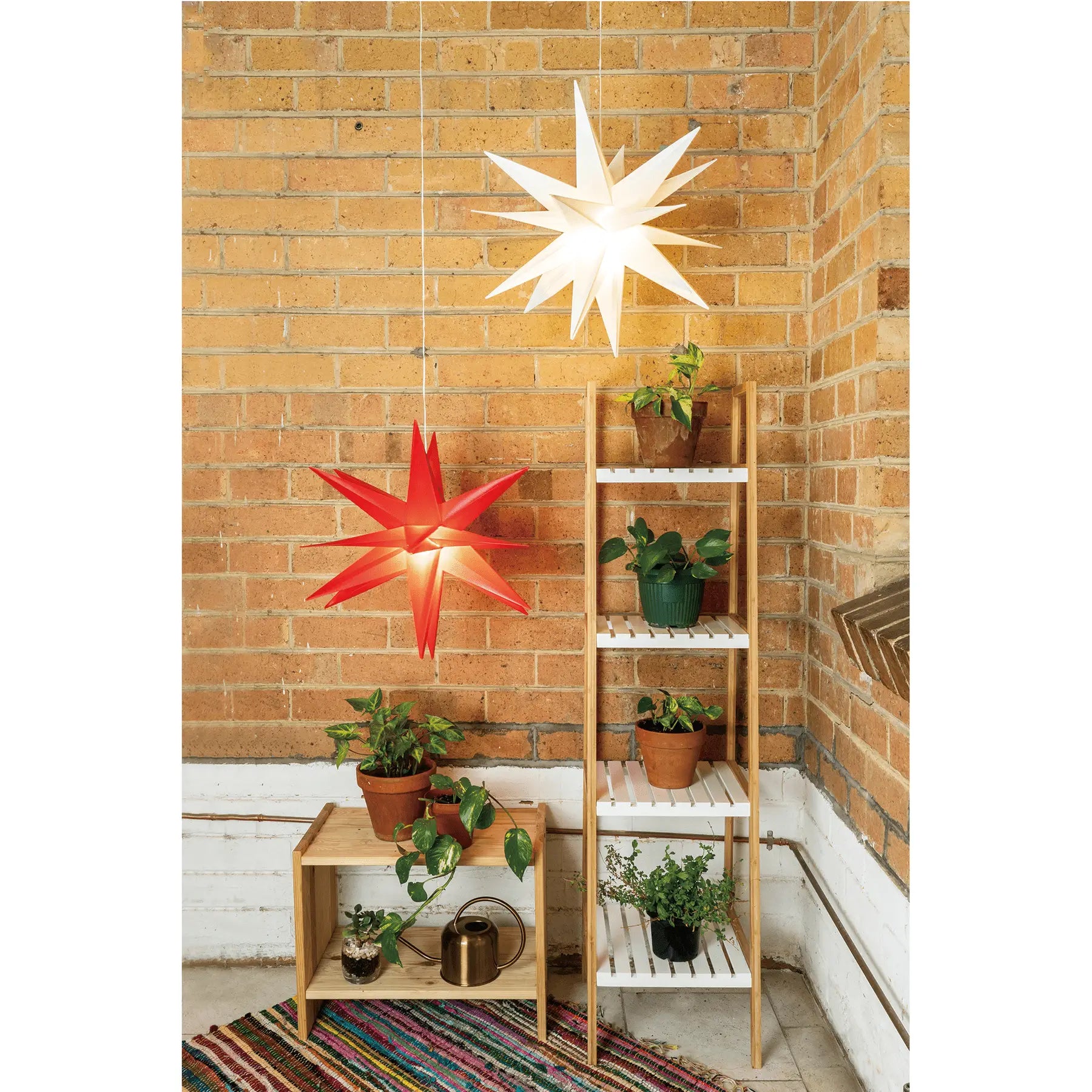 Two starburst hanging light paper lanterns in white and red with plug-in power and colour options against brick wall
