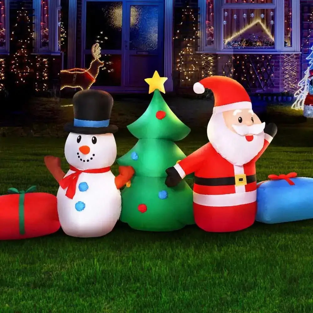 Inflatable Christmas decorations including a snowman, tree, and Santa Claus on grass with festive lights in the background.