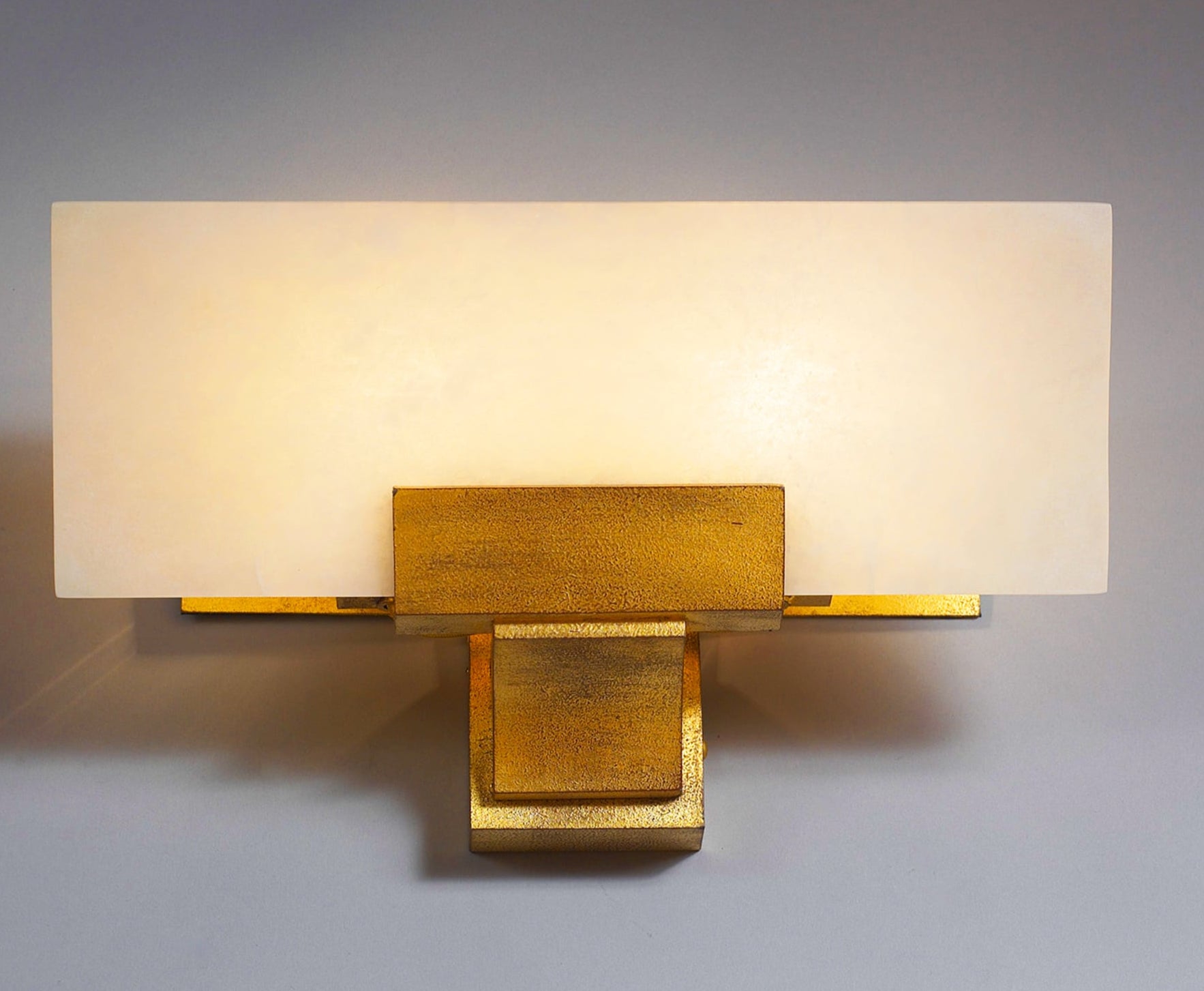 Wall-mounted light fixture with gold base and white shade on a gray background