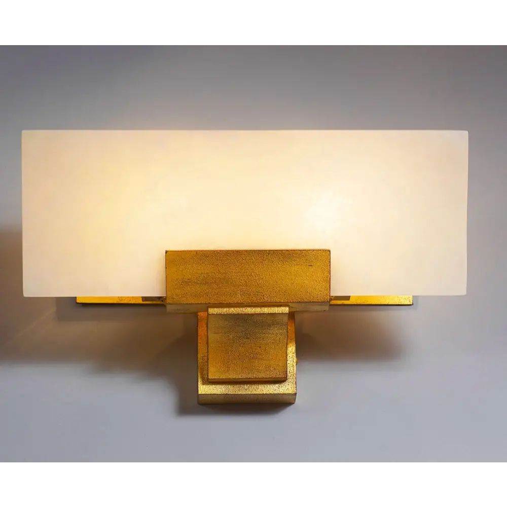 Wall-mounted light fixture with gold base and white shade on a gray background