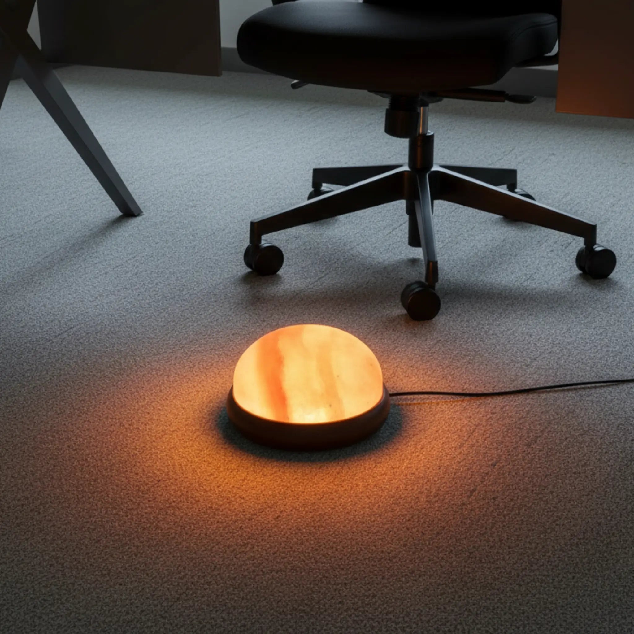 Round salt lamp lamp emitting a warm glow on a carpeted floor with an office chair in the background.